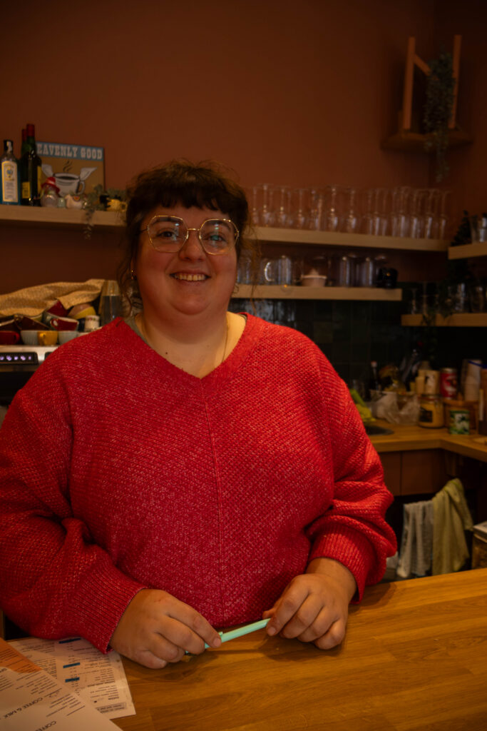Portret foto van een jong volwassen vrouw met bruin haar, een bril en een roos/ rose trui