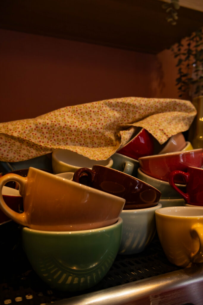 Een foto van allemaal. verschillende koffie tasjes, in verschillende kleuren. de tassen staan een allemaal in en door elkaar. Op de tassen ligt ook een handdoek.