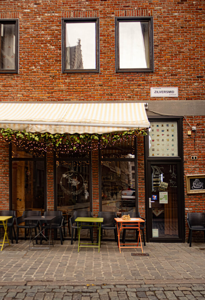 De voorgevel van een coffee shop met kerst lichtjes en 4 tafeltjes vanvoor op de stoep geplaatst.